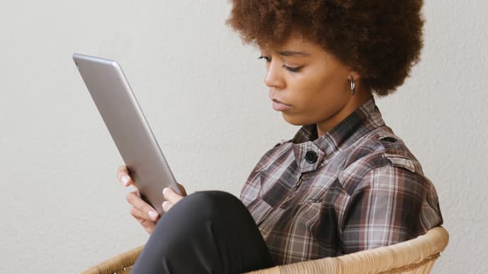 Frau sitzt lesend mit einem iPad auf eine Rattanstuhl