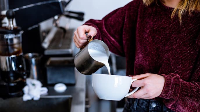 Frau gießt Milch in Tasse