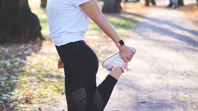 Frau dehnt sich im Wald mit einer Fitbit am Handgelenk