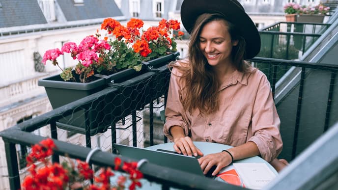 Frau sitzt auf Balkon mit Laptop