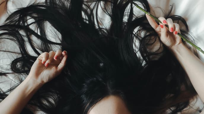 Frau mit schwarzen Haaren liegt auf dem Bett 