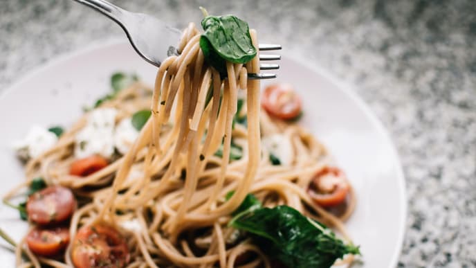 Weißer Teller mit Pasta, Tomaten und Spinat