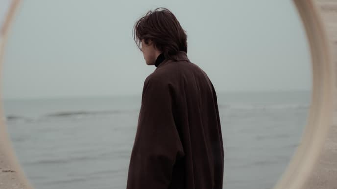 Spiegel am Strand und ein Mann im braunen Mantel ist darin zu sehen