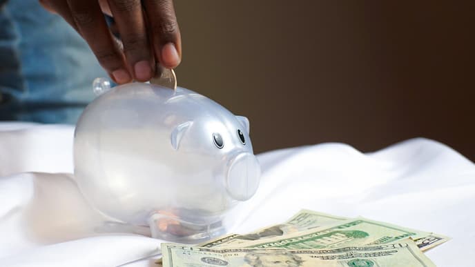 Hand, die Geld in Sparschwein steckt