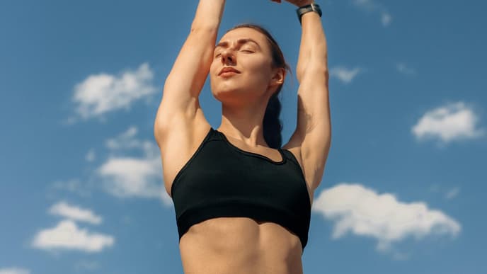 Frau mit Sport-Bh und Sporleggings streckt die Arme in den Himmel