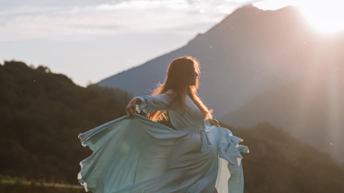 Frau tanzt im Kleid auf der Wiese bei Sonnenschein 