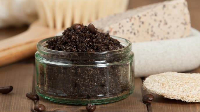 Kaffeepeeling im Glas, dahinter Seife und eine Trockenbürste