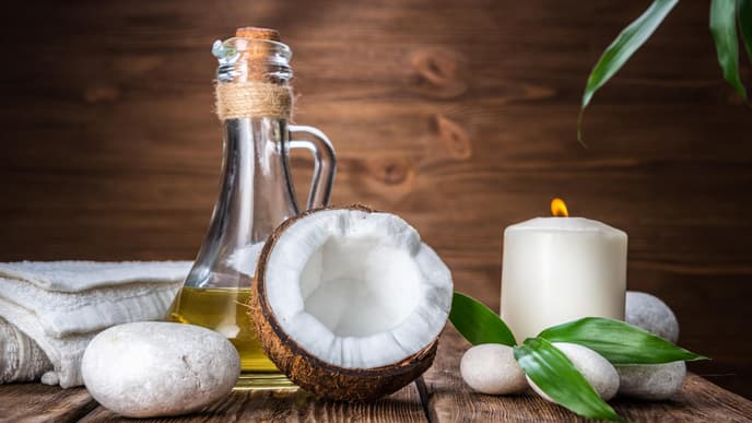 Kokosöl Haare: Ölflasche steht neben einer halben Kokosnuss und einer Kerze auf einem Tisch