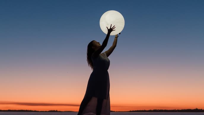 Horoskop: Frau hält einen Vollmond in der Hand am Strand