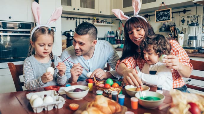 Warum feiern wir Ostern? Familie sitzt am Tisch und bemalt Ostereier