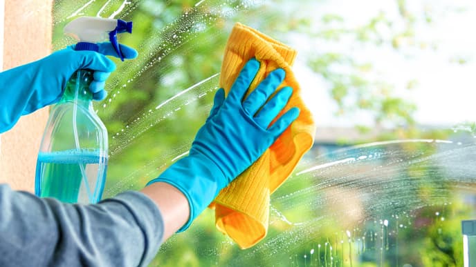 Fenster putzen: Hände mit Putzhandschuhen säubern eine Fensterscheibe