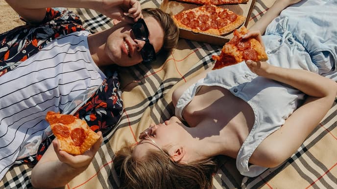 Horoskop: Mann und Frau liegen auf Decke mit Pizza