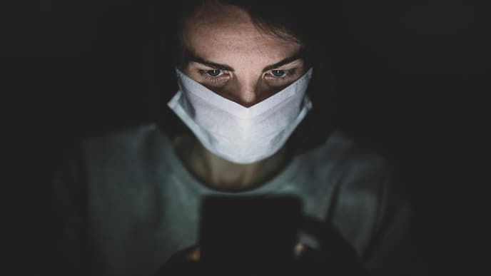 Person mit Mund- und Nasenschutz schaut auf Handy