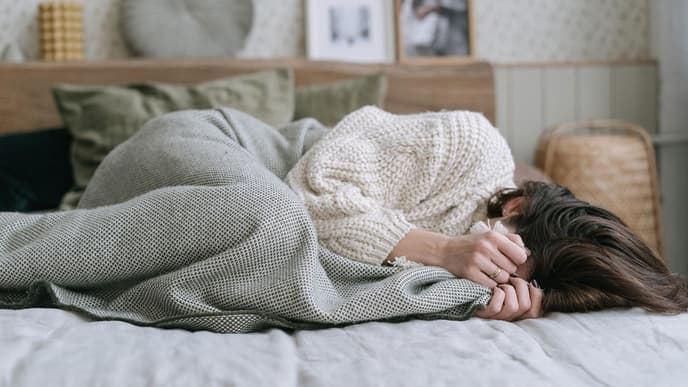 Frau im Bett mit Händen vor Gesicht 