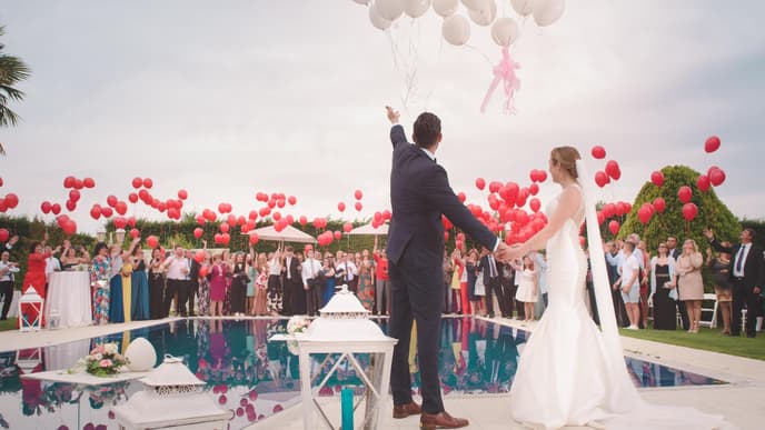 Brautpaar steht vor Pool und lässt Luftballons steigen