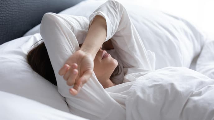 Frau rauft Arme über den Kopf zusammen und liegt im Bett