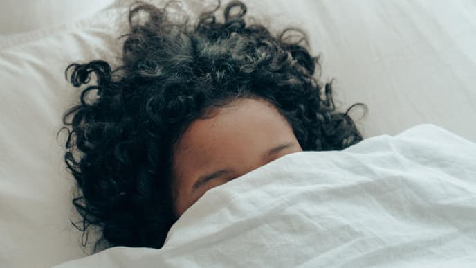 Frau im Bett mit Decke über dem Kopf