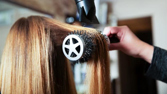 Frau werden die Haare auf einer Rundbürste geföhnt