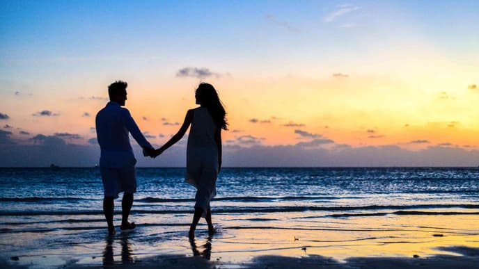 Frau und Mann halten Händchen und spazieren am Strand