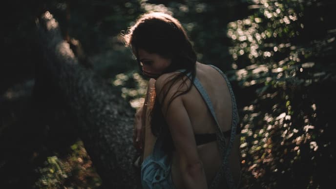 Frau im Wald guckt traurig zur Seite 