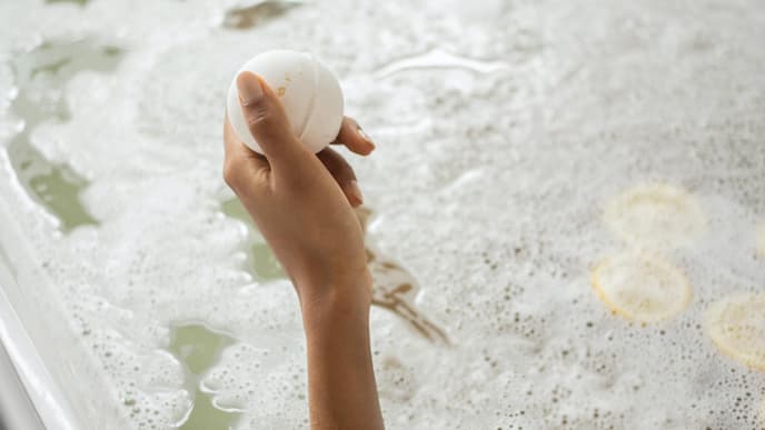 Badekugel in Hand und Badewanne