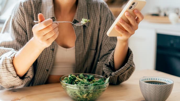 Frau isst Salat mit Smartphone in der Hand