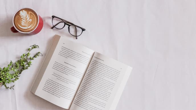 Buch liegt neben Brille und Kaffee