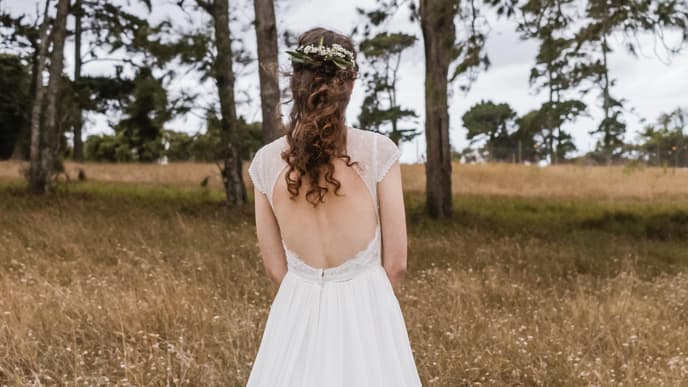 Frau mit Boho Hochzeitsfrisur steht auf einem Feld mit dem Rücken zur Kamera.