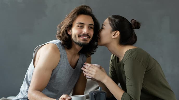 Mann und Frau sitzen auf einem Bett und trinken Kaffee