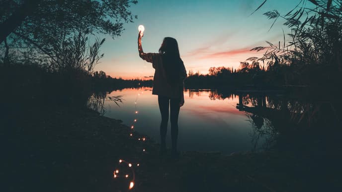 Frau am See hält eine Glühbirne mit einer Lichterkette in der Hand.