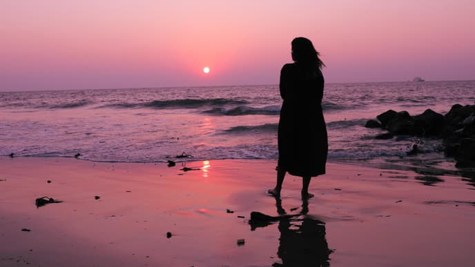 Frau steht am Strand und schaut den Himmel an
