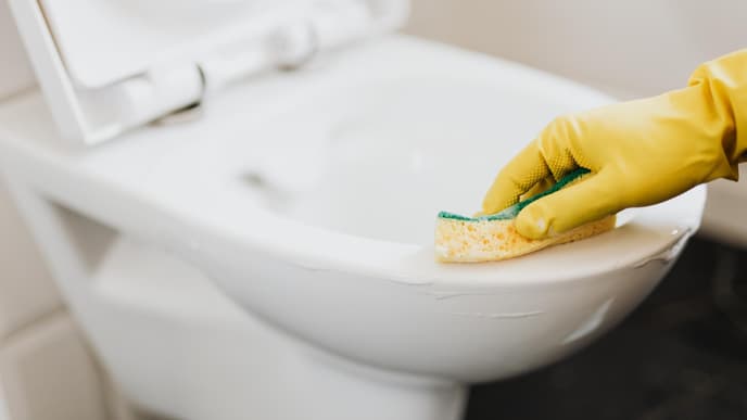Person putzt eine weiße Toilette mit einem gelben Schwamm
