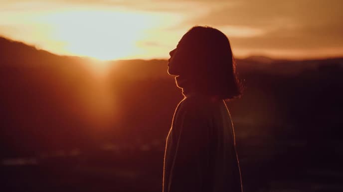Frau mit kurzen Haaren steht vor einem Sonnenuntergang