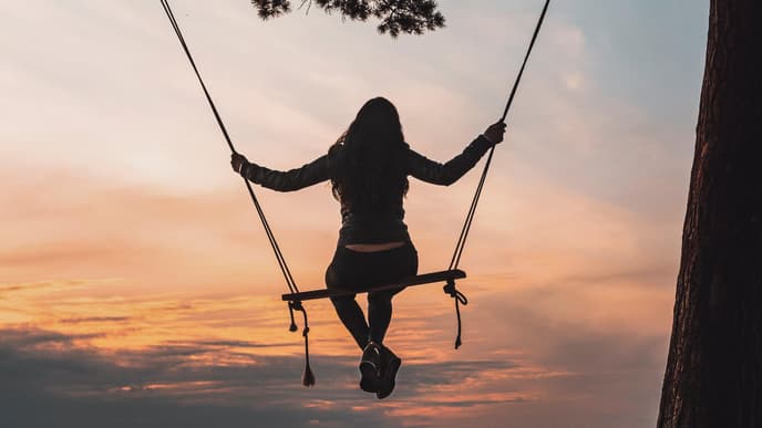 Frau auf einer Schaukel beim Sonnenaufgang