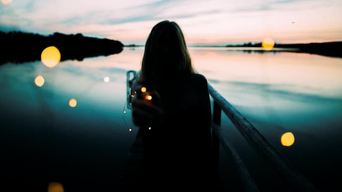 Frau steht am See mit einer Lichterkette