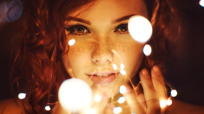 Frau mit Sommersprossen und Eyeliner hält eine Lichterkette in der Hand