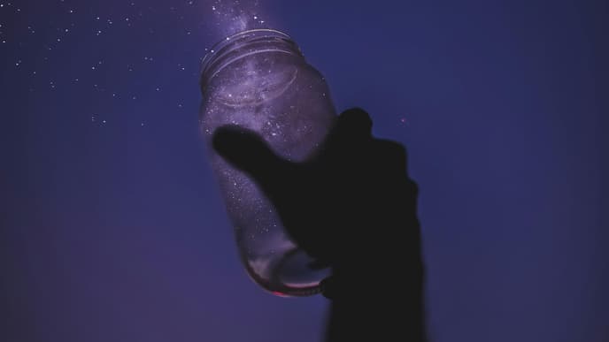 Hand hält ein Glas mit Sternen in die Luft 