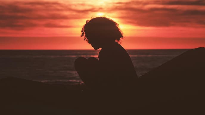 Frau sitzt beim Sonnenuntergang am Meer