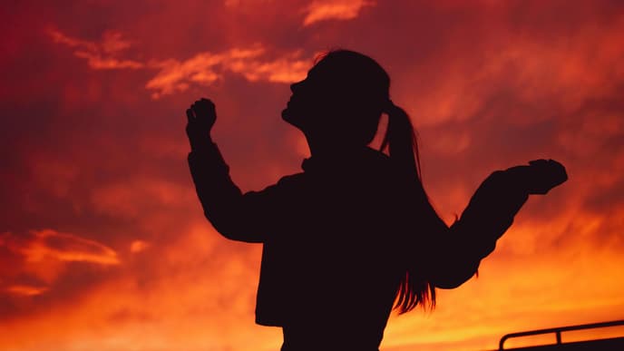 Silhouette einer Frau mit Zopf vor einem roten Himmel