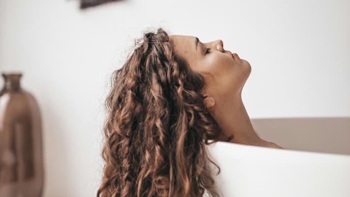 Dicke Haare: Frau liegt in Wanne mit braunen Locken