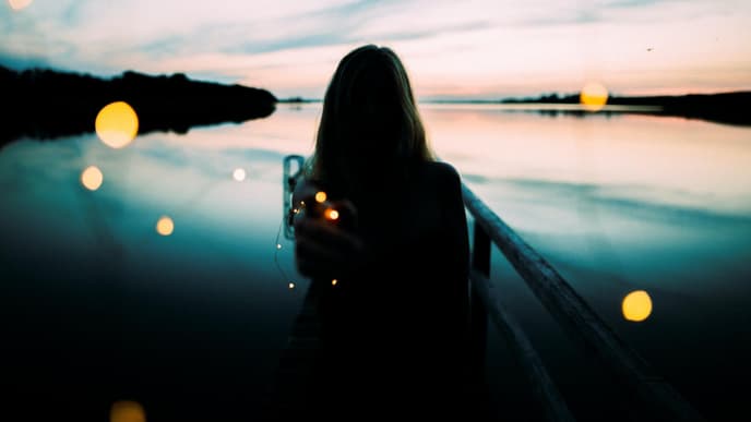 Frau steht am See mit einer Lichterkette