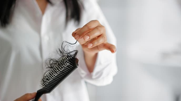 Eine Frau hält eine Bürste mit ihren ausgefallenen Haaren in der Hand