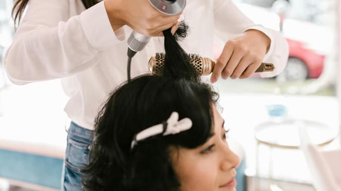 Friseurin stylt Haare der Kundin mit Föhn und Rundbürste