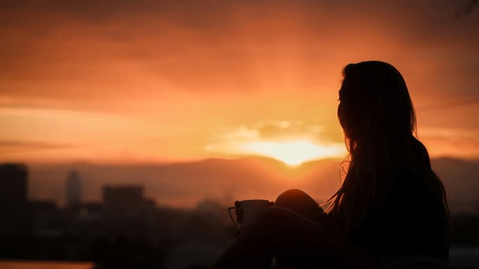 Frau sitzt vor Abendhimmel