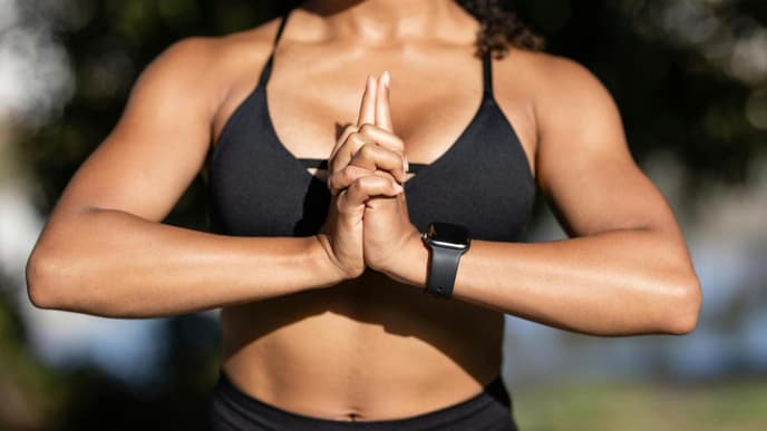 Der Oberkörper einer Frau mit einem schwarzen Sport-BH, die ihre Hände vor der Brust zusammendrückt.