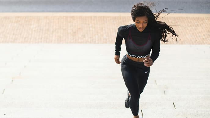 Laufen ist 2026 nach wie vor ein großes Thema. Frau in schwarzem Sport-Outfit läuft draußen Treppenstufen hoch.