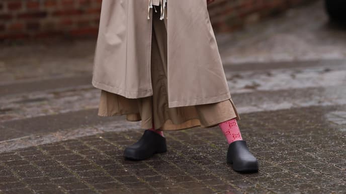 Frau im beigen Mantel mit Garden Shoes und einer weinroten Tasche.