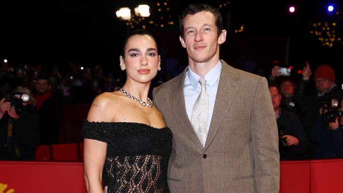 Dua Lipa in einem schwarzen Spitzenkleid und Callum Turner in einem braunen Anzug.