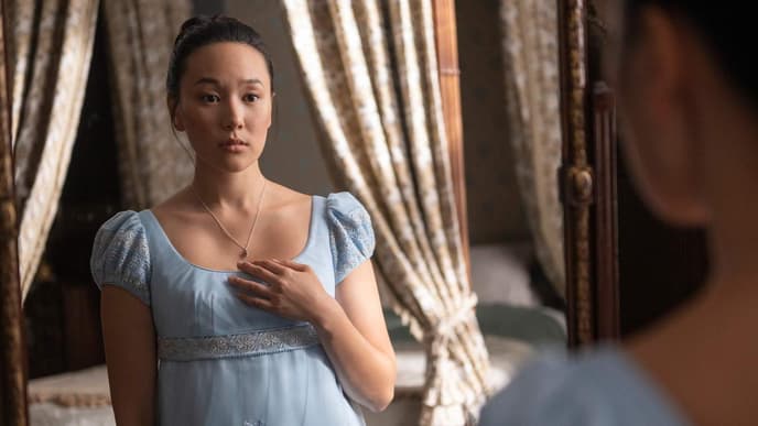 Eine junge Frau in einem babyblauen Kleid guckt starr nach vorn und fasst sich an ihr Dekollete.