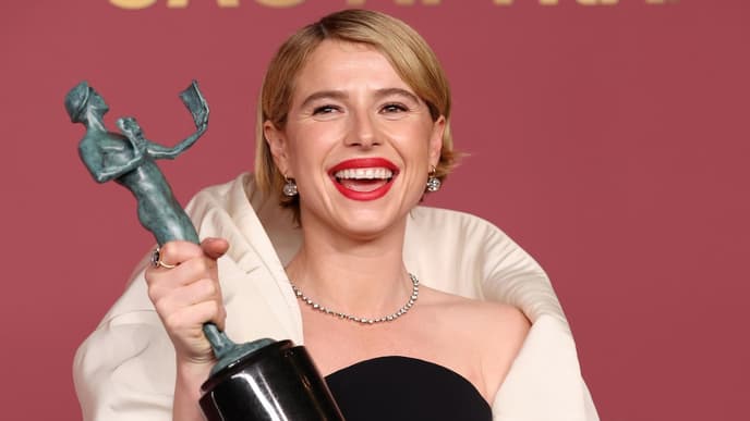 Jessie Buckley mit einem Award in der Hand strahlt in die Kamera.
